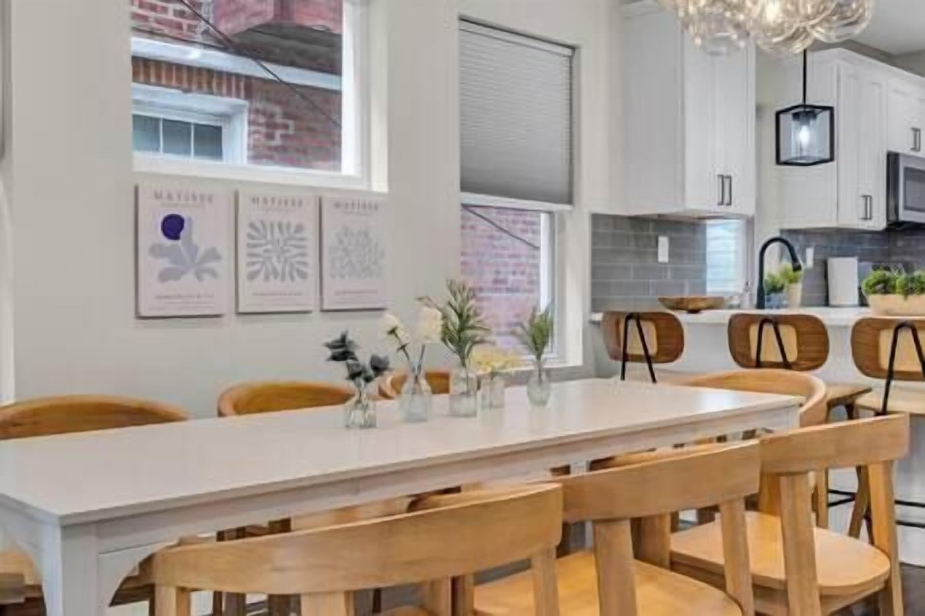 A modern kitchen with white cabinets, a long dining table, and wooden chairs.