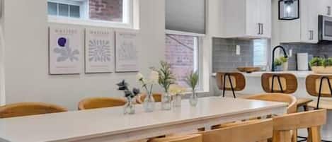 A modern kitchen with white cabinets, a long dining table, and wooden chairs.