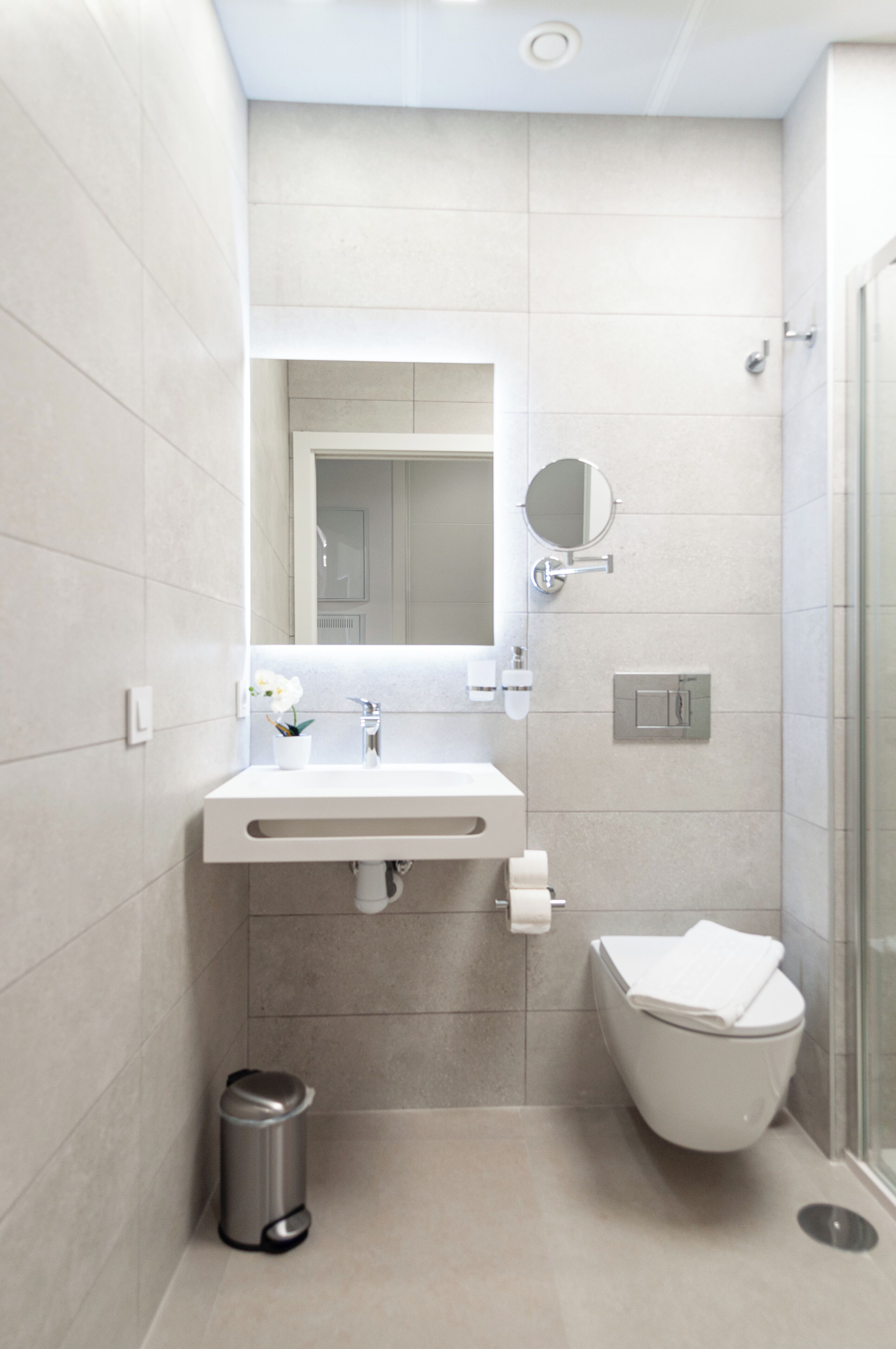 Un baño moderno con un lavabo blanco, espejo, inodoro y cubo de basura.