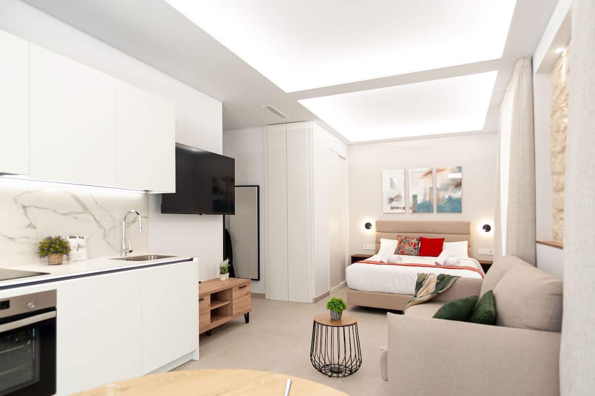 En modern lägenhet med kök, matplats och ett sovrum med säng, soffa och TV.