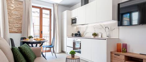 Una cocina moderna con armarios blancos, microondas y televisor sobre la encimera.