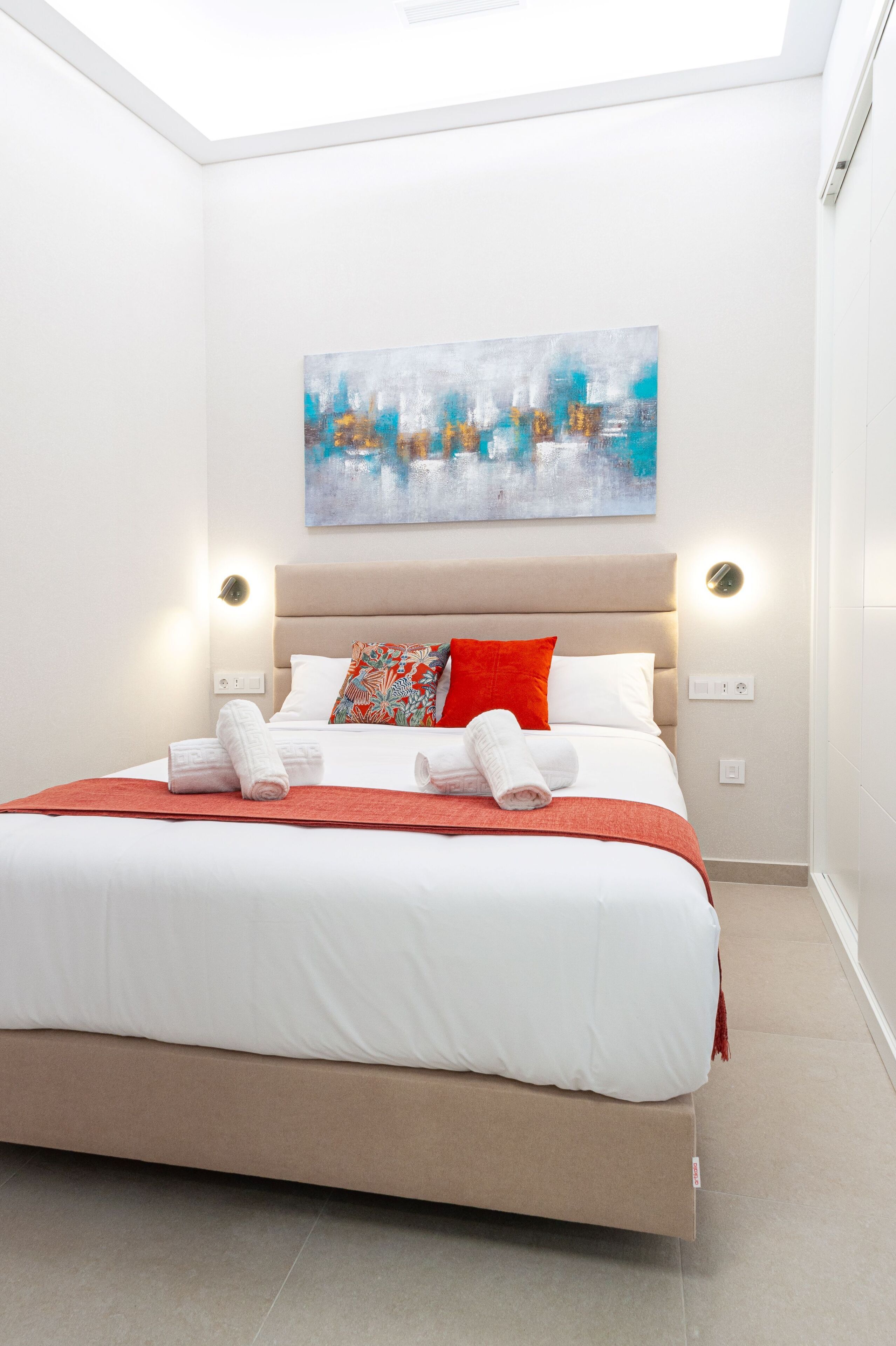 A modern hotel room with a large bed, a painting on the wall, and two bedside lamps.