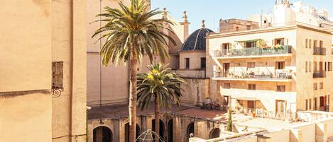 Una terraza en la azotea con palmeras, una torre de campanas y edificios adyacentes.