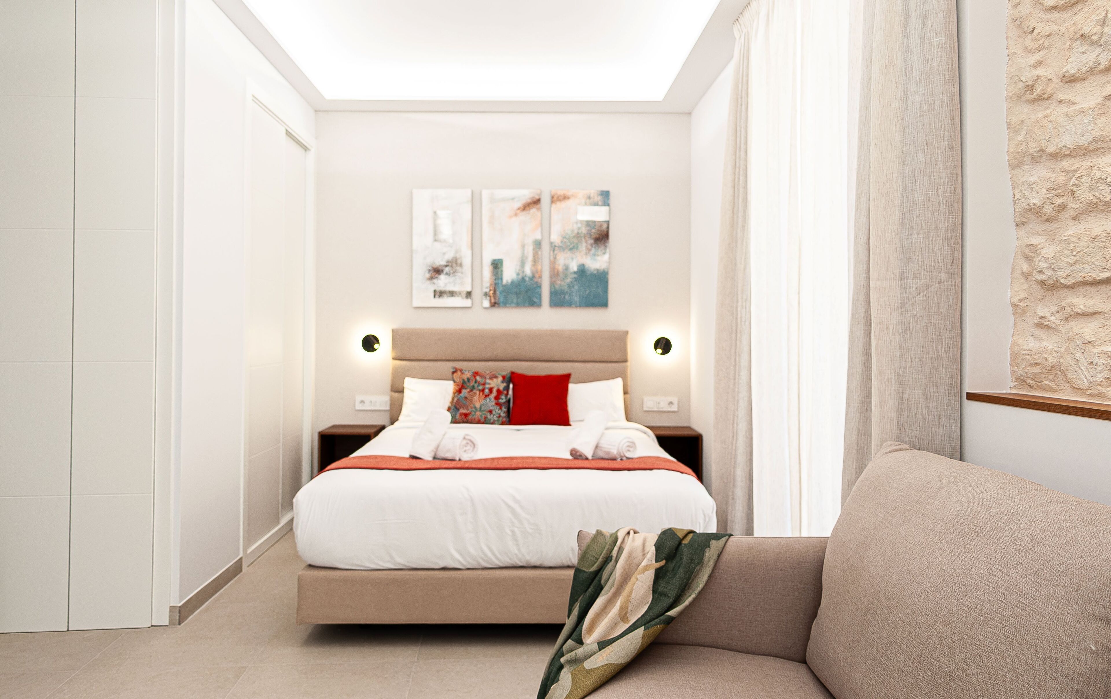 A modern hotel room with a large bed, a sofa, and artwork on the wall.