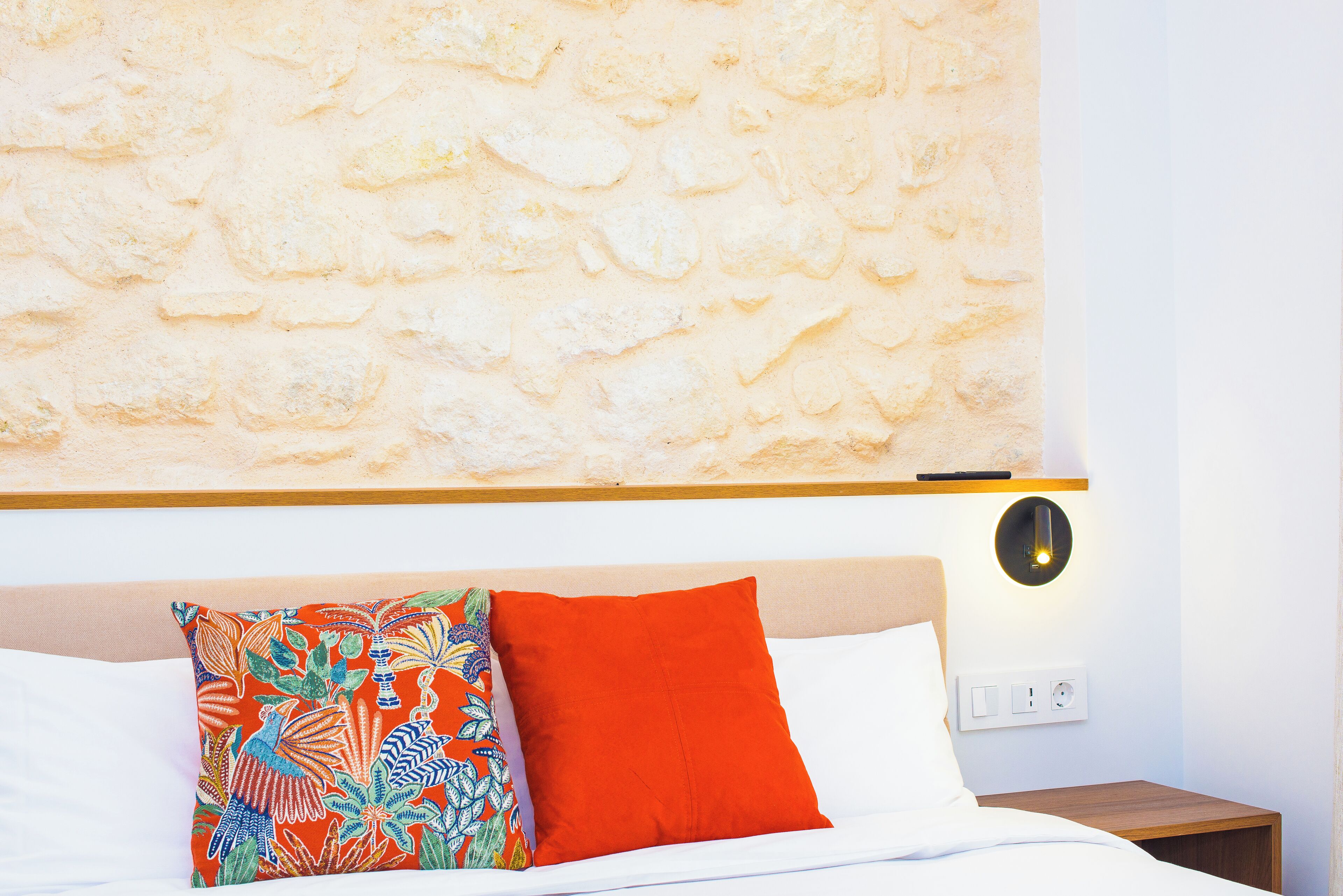 A bed with white linens, a wooden headboard, a nightstand, and a wall with a textured stone pattern.