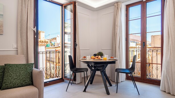 A dining area with a table set for two, a sofa with a cushion, and a view through a glass door to the outside. - Myflats Luxury Cathedral (Alicante)