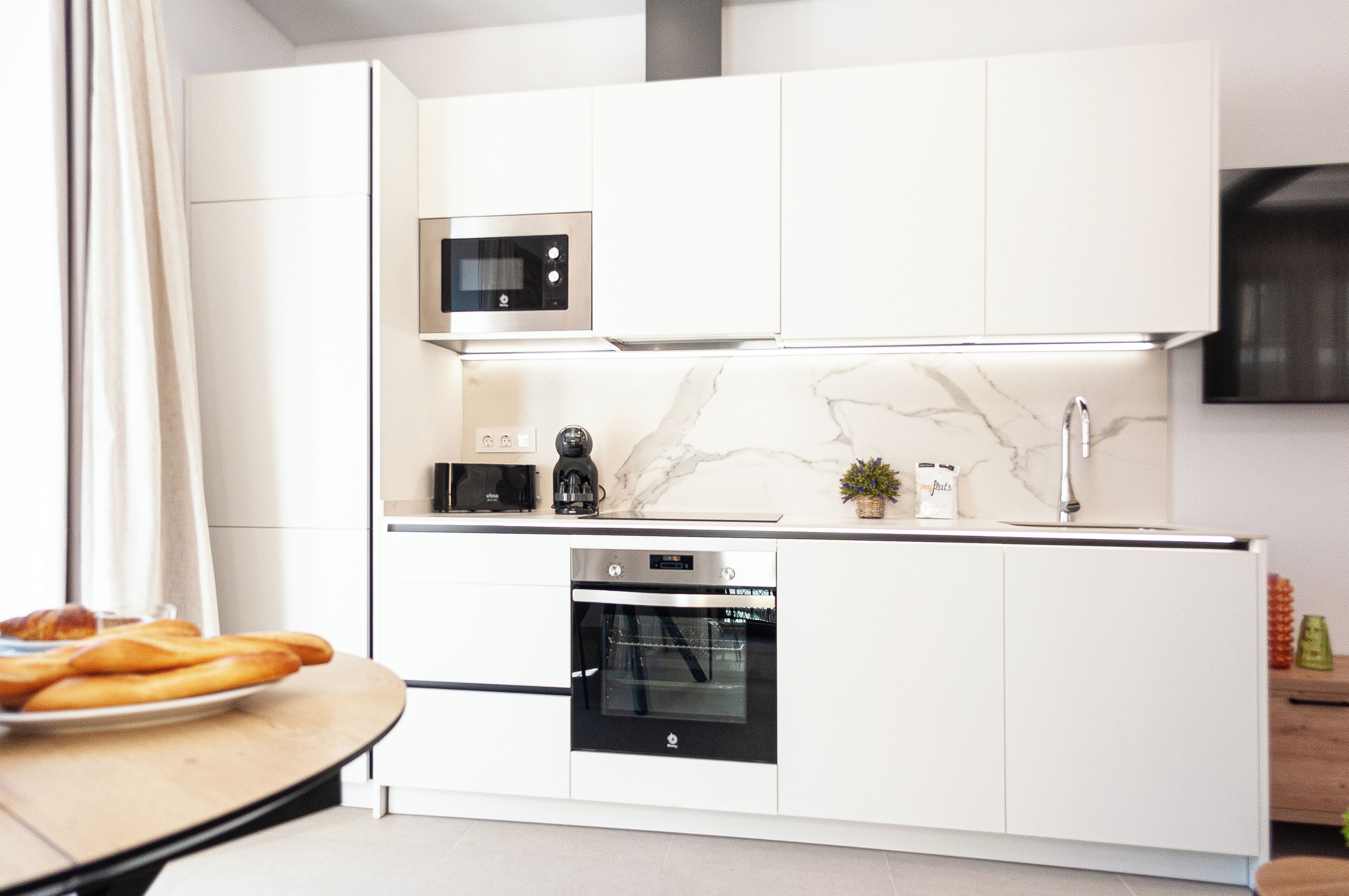A modern kitchen with white cabinetry, a built-in oven, a microwave, and a marble backsplash.
