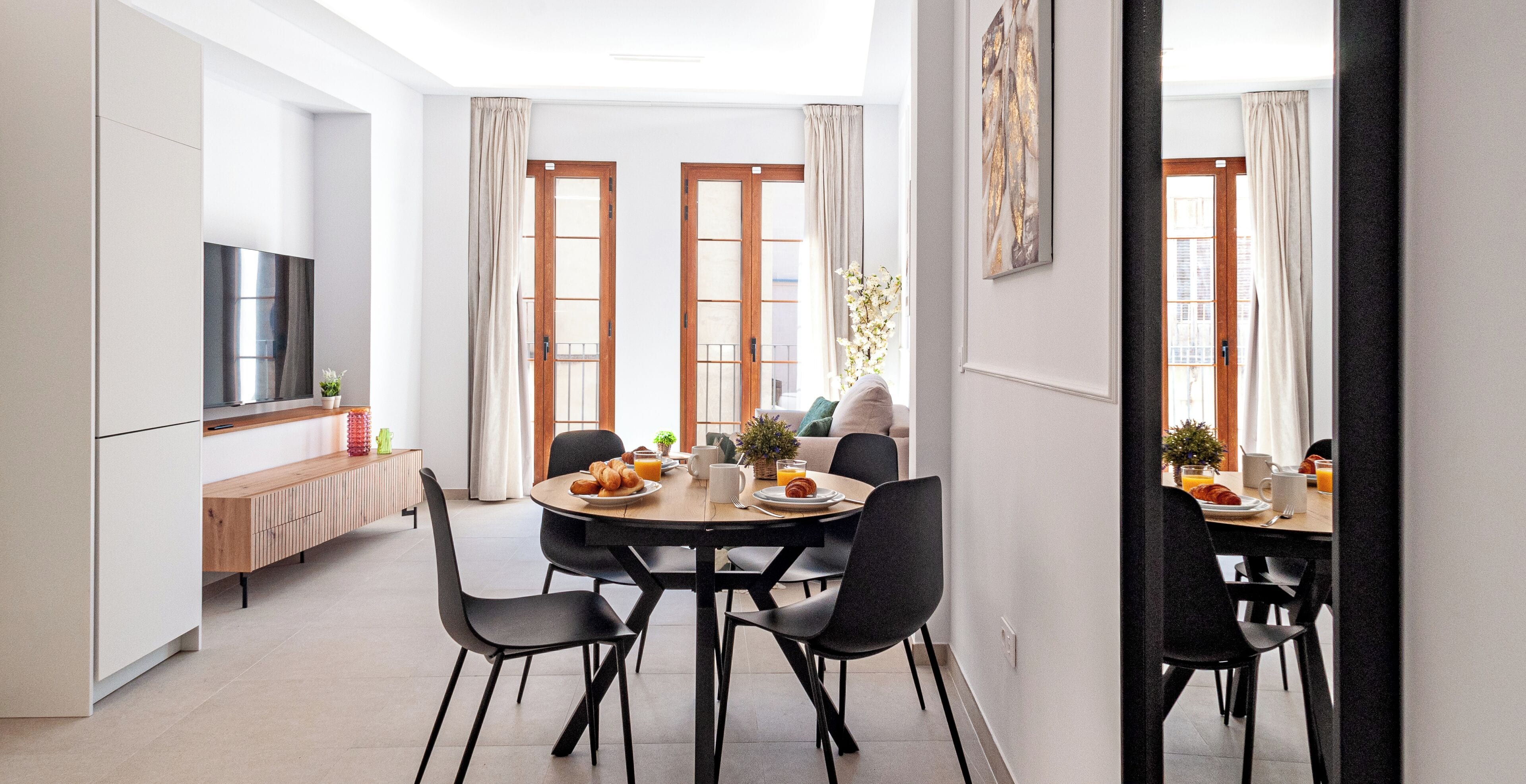 A modern dining area with a round table, black chairs, and a TV on the left.
