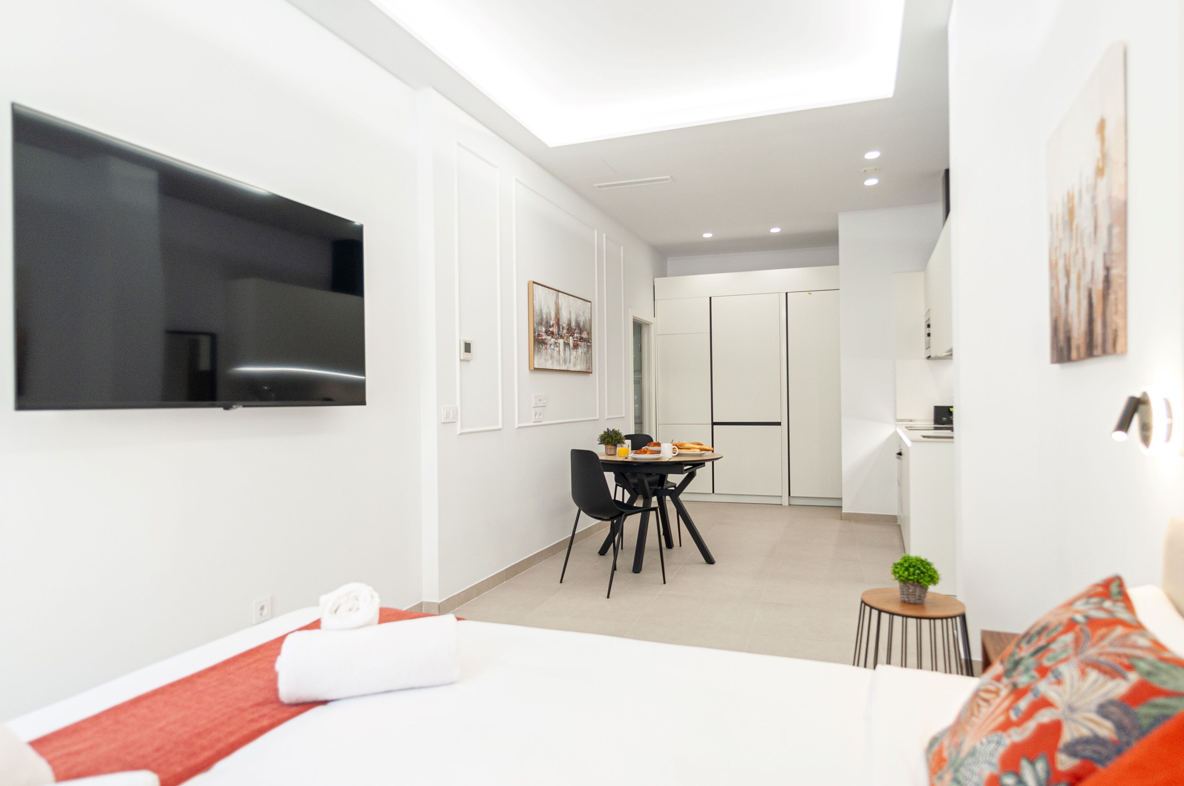 Quarto de hotel moderno com cama, área de refeições e cozinha compacta.