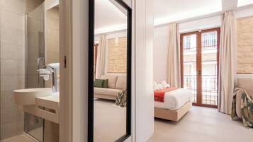 A modern hotel room with a large mirror, a bathroom with a sink and shower, a bed with a red blanket, and a balcony with a view.