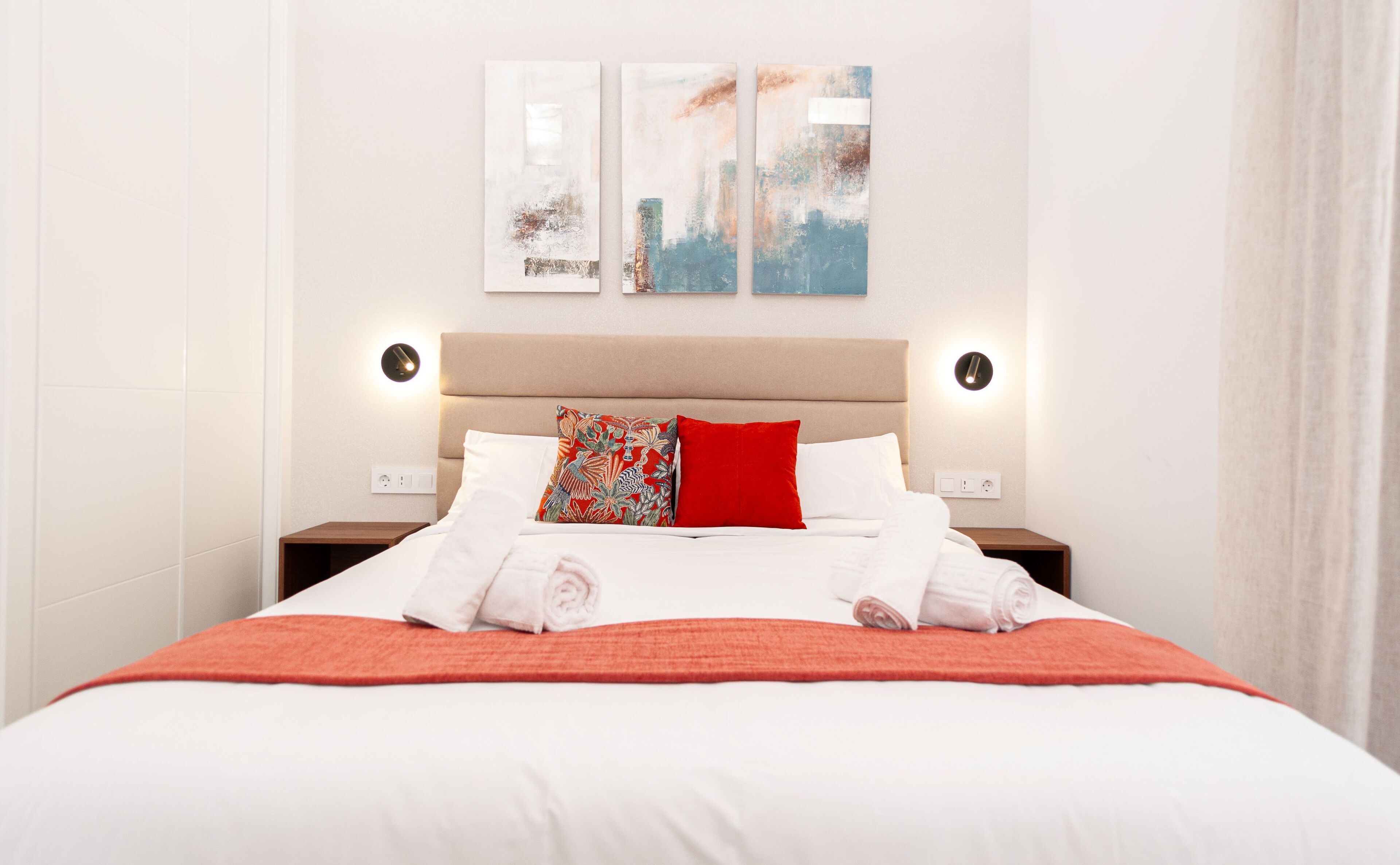 A hotel room with a large bed, two bedside tables, a headboard, and two wall-mounted light fixtures.