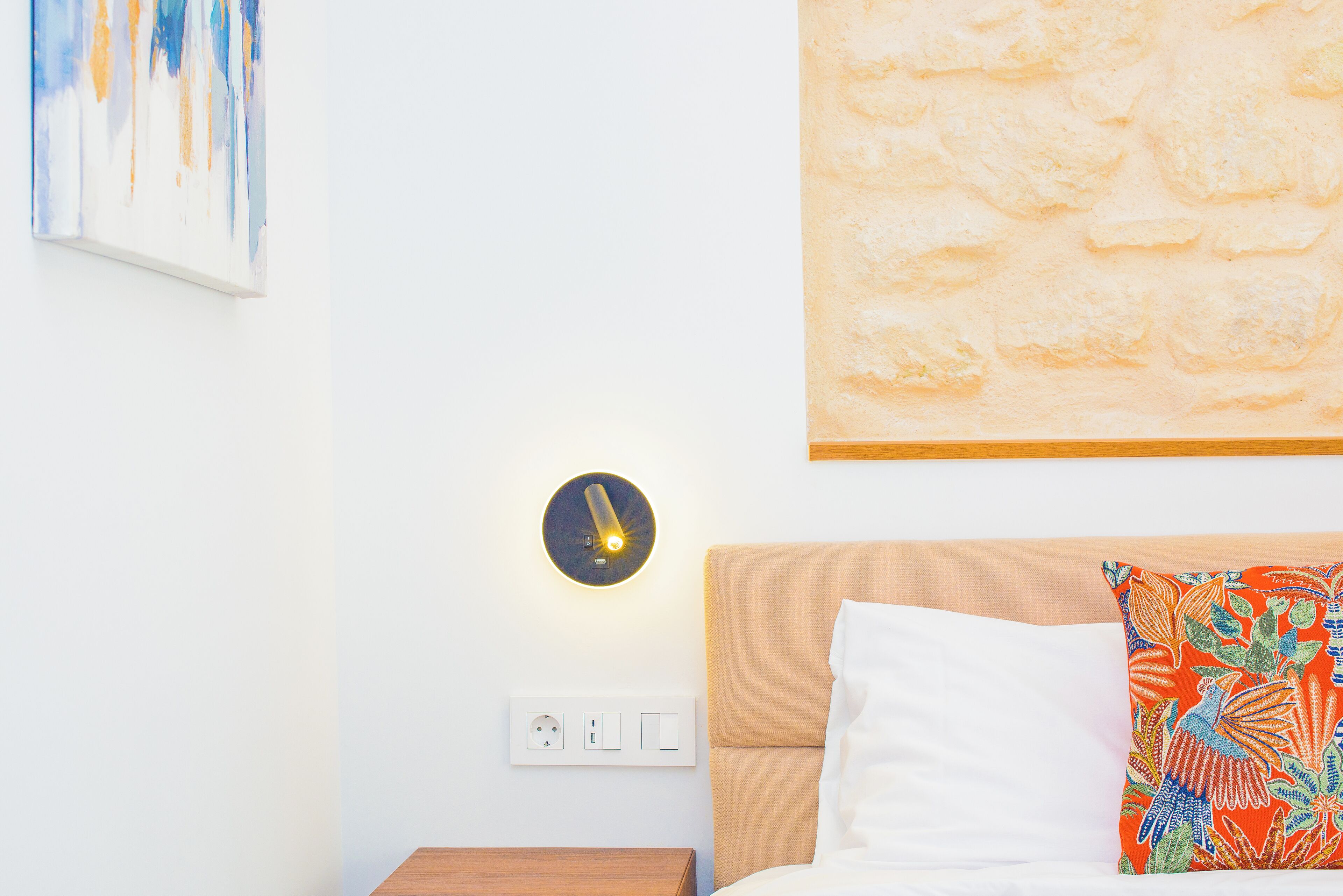 A hotel room with a bed, a nightstand, a wall clock, and a power outlet.