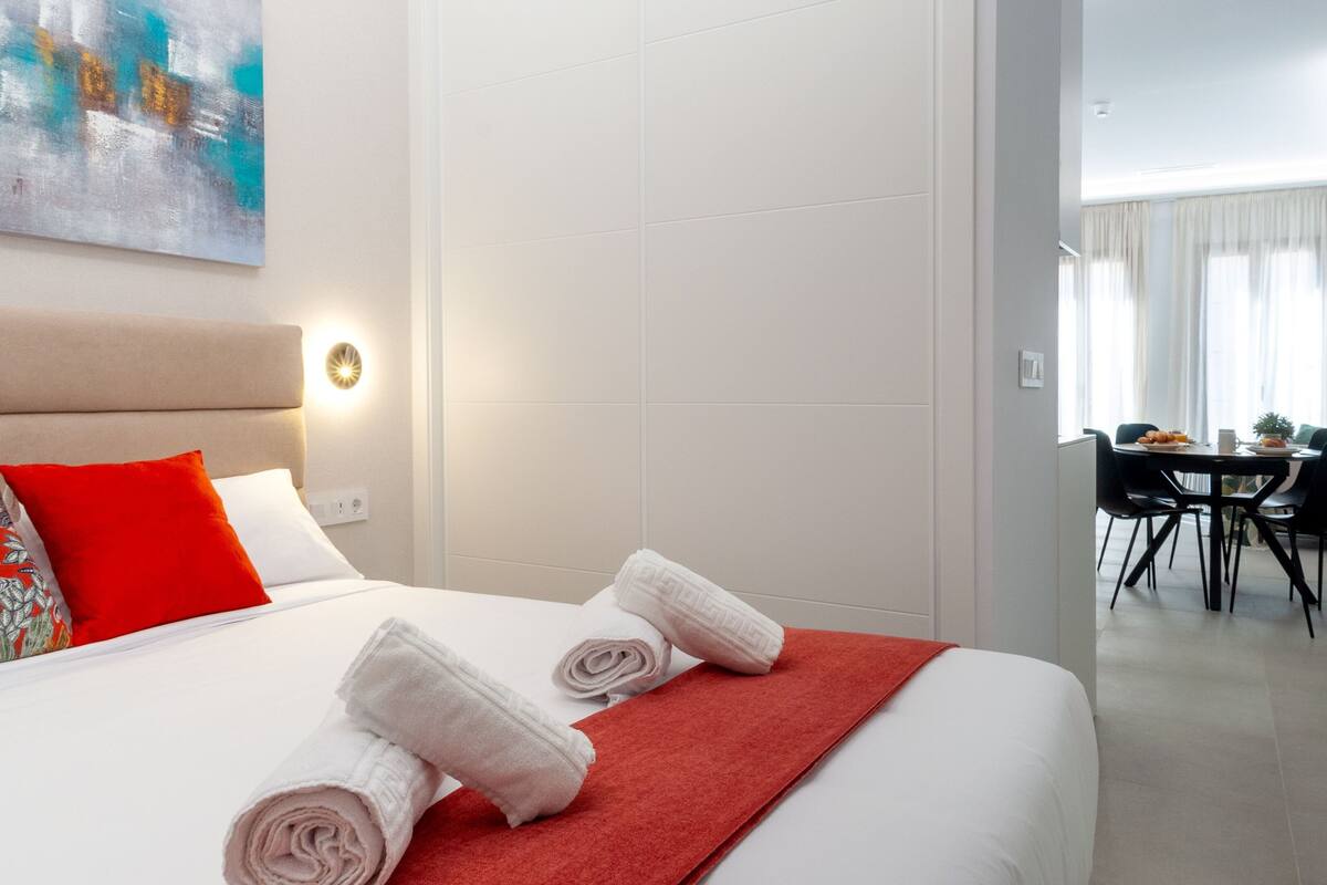 Ett hotellrum med en säng, en röd pläd och en tavla på väggen.
