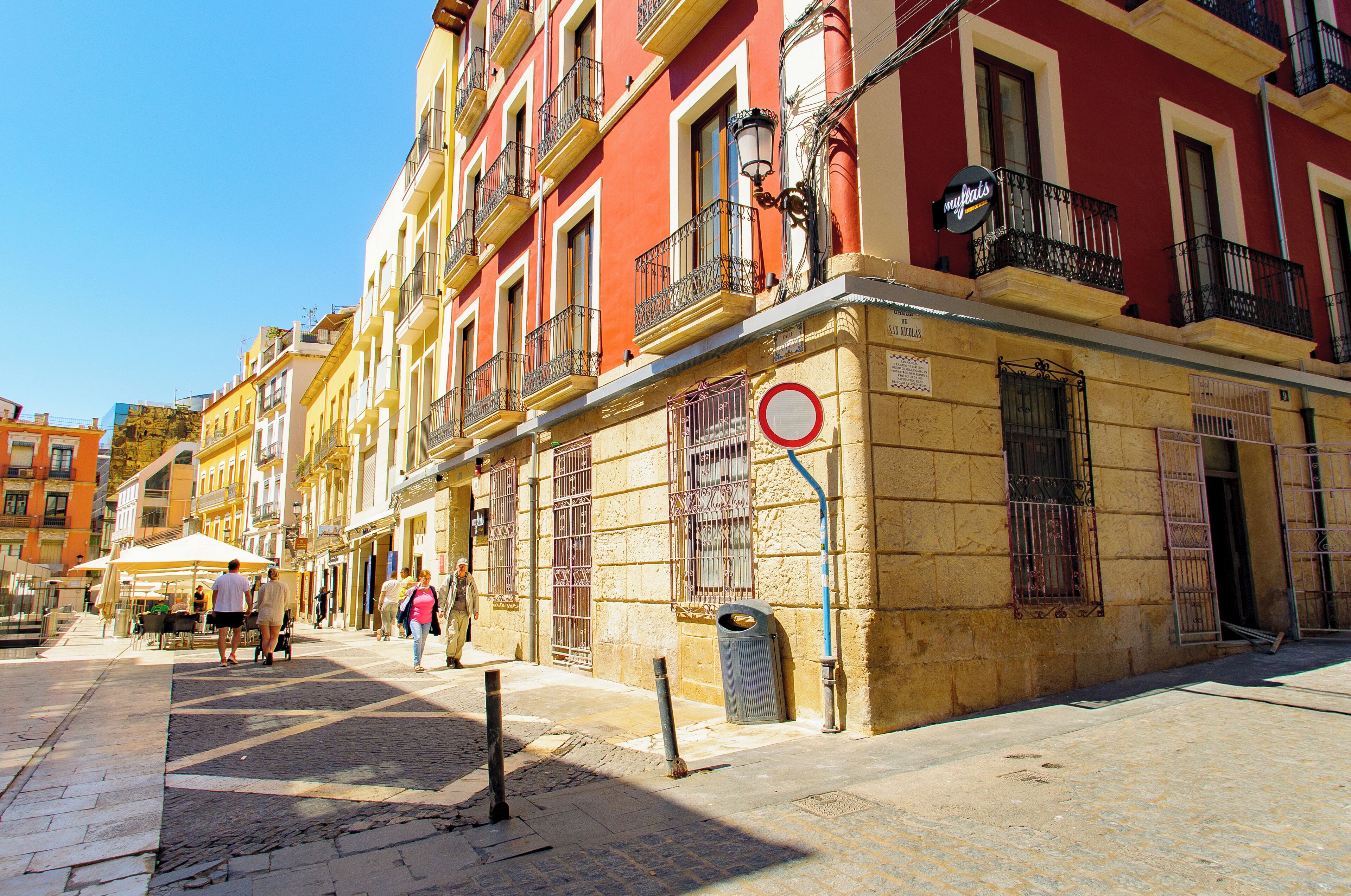 A street with buildings, a trash bin, and people walking.