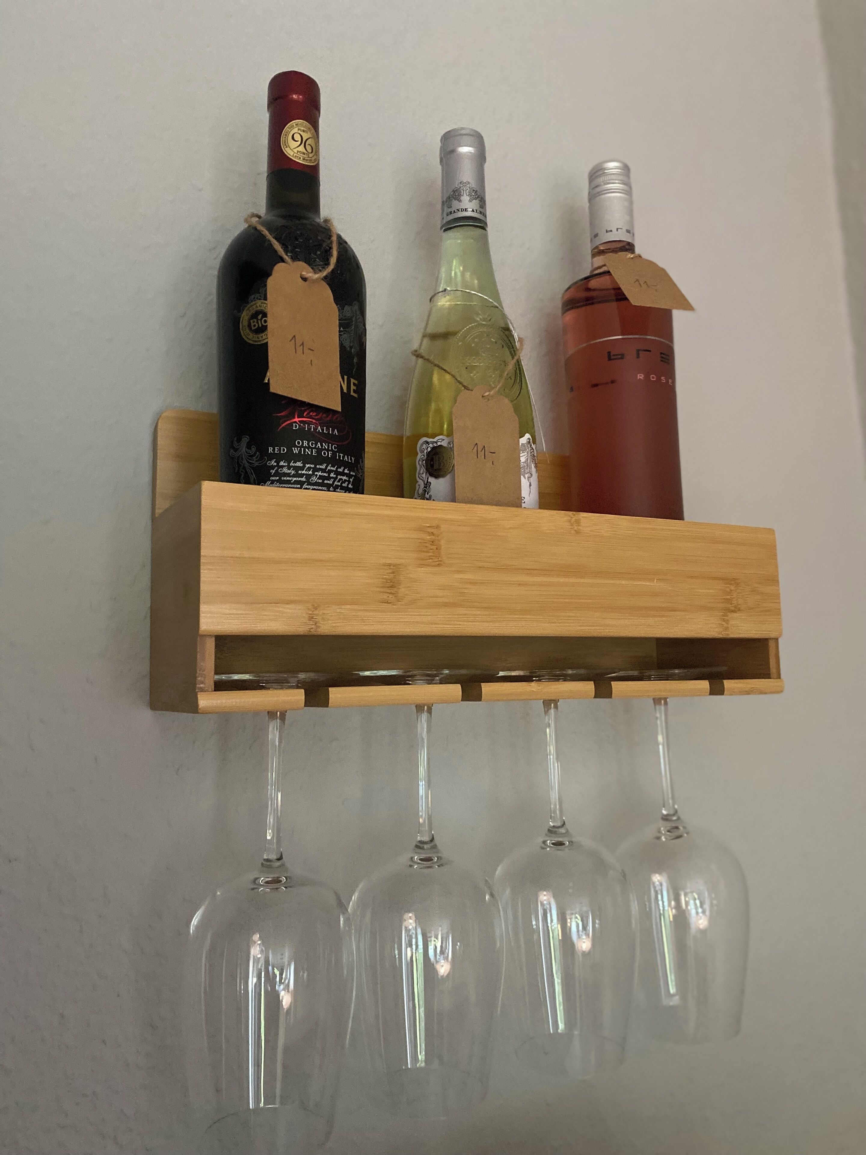 A wooden wine rack with three bottles and four wine glasses.