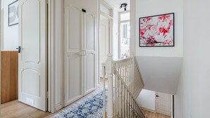 Un pasillo con puertas blancas, un tapete de diseño azul y una escalera con barandilla blanca.