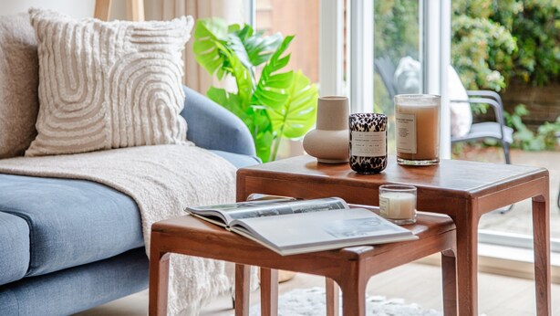 Una sala de estar acogedora con un sofá azul, una mesa de centro de madera con una revista, velas y una planta.