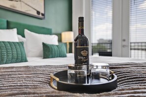A bottle of Stella Rosé on a tray on a bed with a green headboard and pillows. - Intimate Flat w/ Pool, Gym, & Stunning City Views (Birmingham)