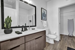 A modern bathroom with a large mirror, white sink, and toilet. There is a potted plant on the vanity and a towel rack with towels. - Intimate Flat w/ Pool, Gym, & Stunning City Views (Birmingham)