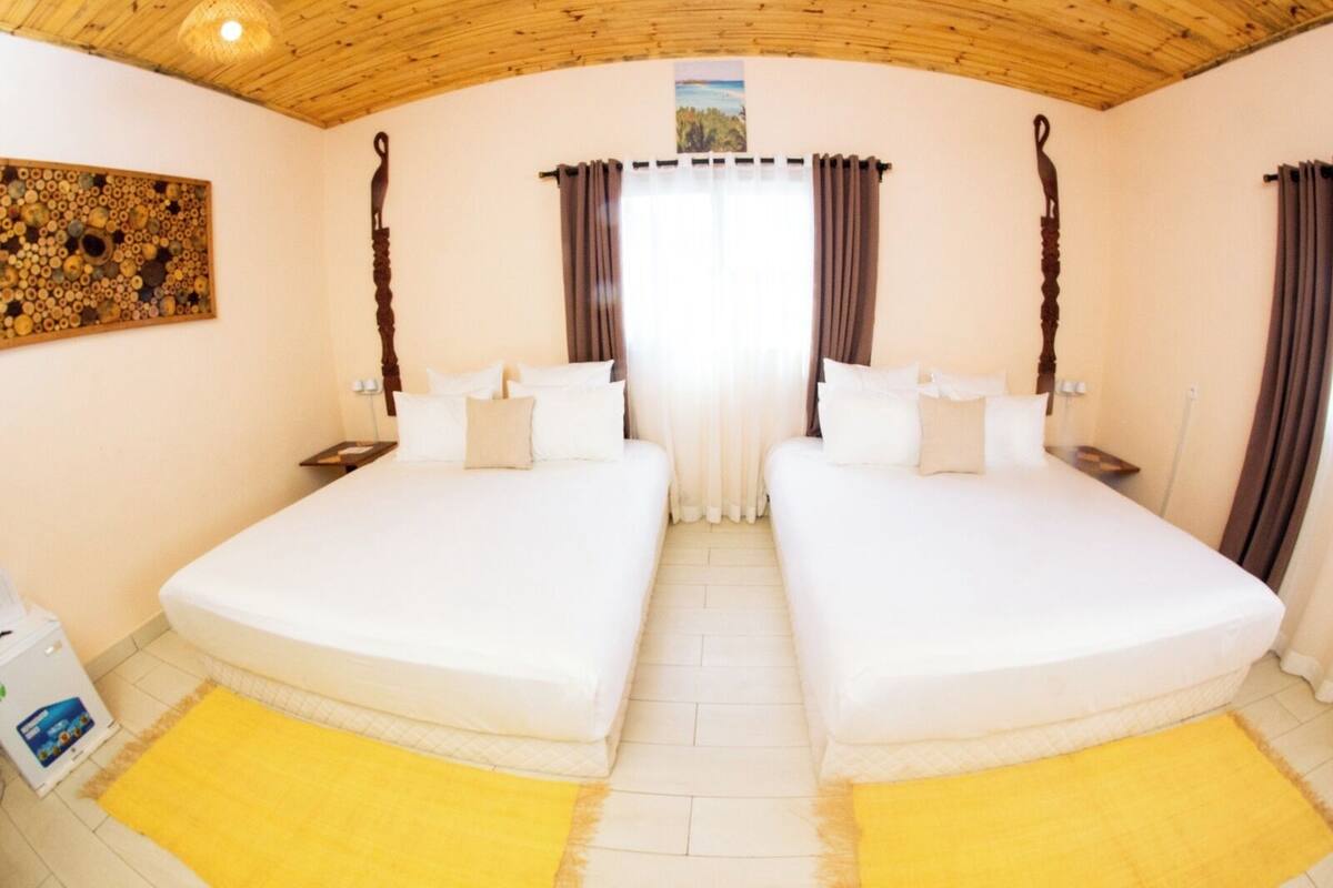 A double room with two beds, a wooden ceiling, and a large window with curtains.