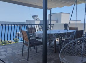 A covered outdoor seating area with a table and chairs, overlooking a body of water. - Bernard Sea View Apartments (Rogoznica)