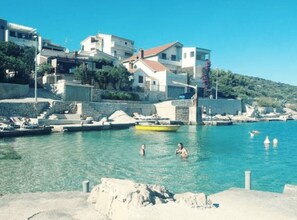 A coastal town with buildings along the waterfront, clear blue water, and people swimming. - Bernard Sea View Apartments (Rogoznica)