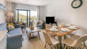 A modern living room with a dining area, large windows, and a view of the landscape.