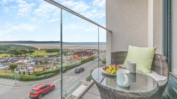 Un balcon avec une table en verre, un fauteuil en osier et une vue sur une ville côtière.