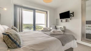 A hotel room with a large bed, a flat-screen TV, a desk, and a view of the outdoors.