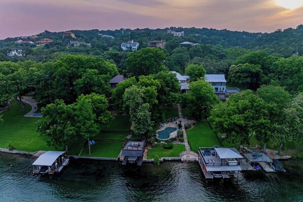 A lakeside property with multiple docked boats, a swimming pool, and a well-maintained lawn. - Lakeside Retreat | Fire Pit, Game Room & Canoe (Austin)