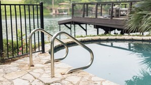 Een stenen zwembad met metalen leuningen en een houten terras op de achtergrond.