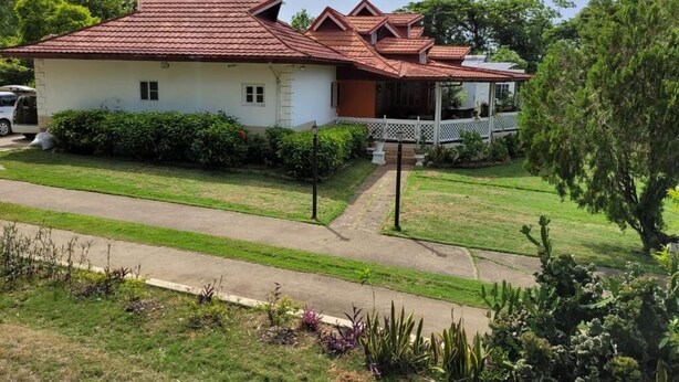 Ein zweistöckiges Haus mit rotem Ziegeldach, einer Veranda mit weißem Geländer und einem gepflegten Rasen.