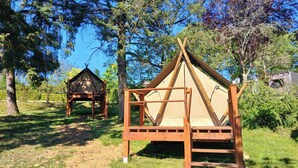 Dos tiendas de madera de diseño sencillo, ubicadas en un área cubierta de césped con árboles al fondo.