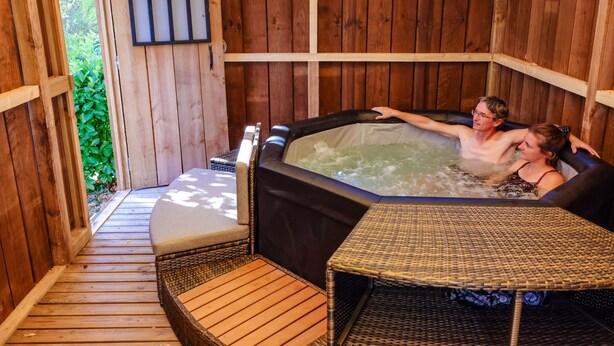 Una cabaña de madera con jacuzzi y mobiliario de mimbre.