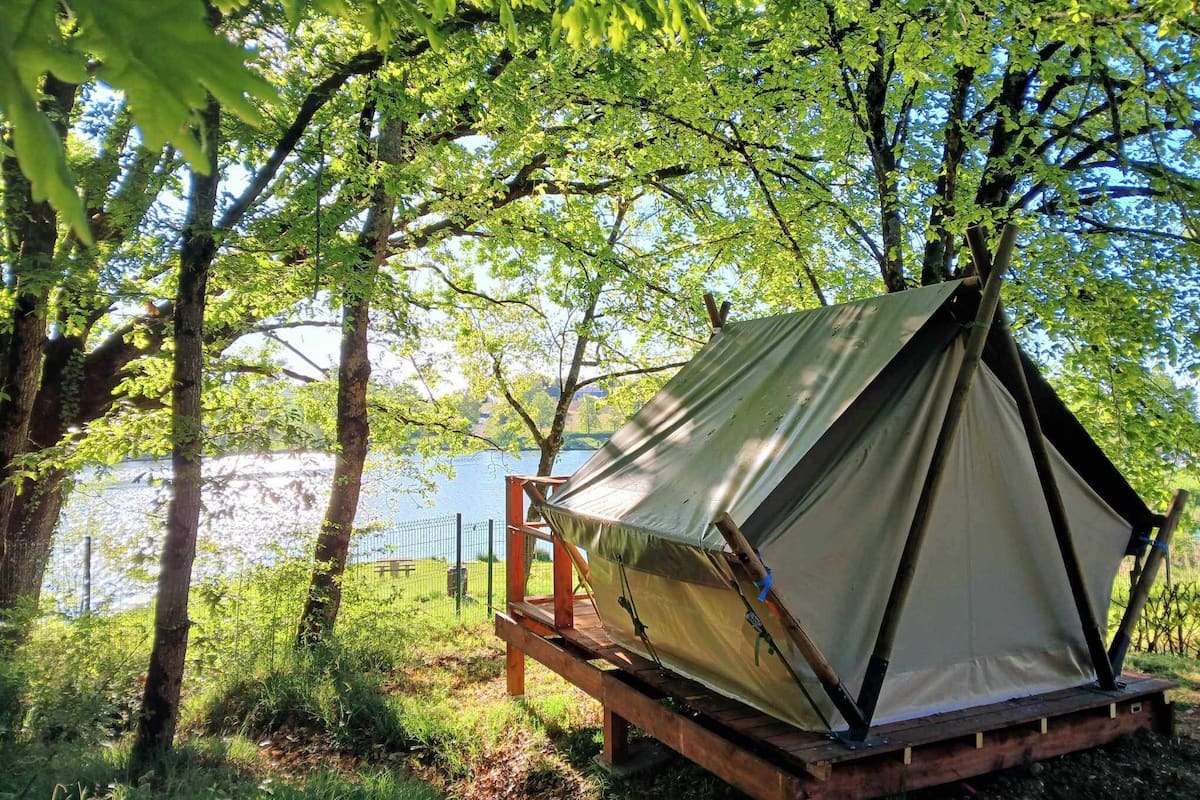 A tent set up in a wooded area with a lake in the background.