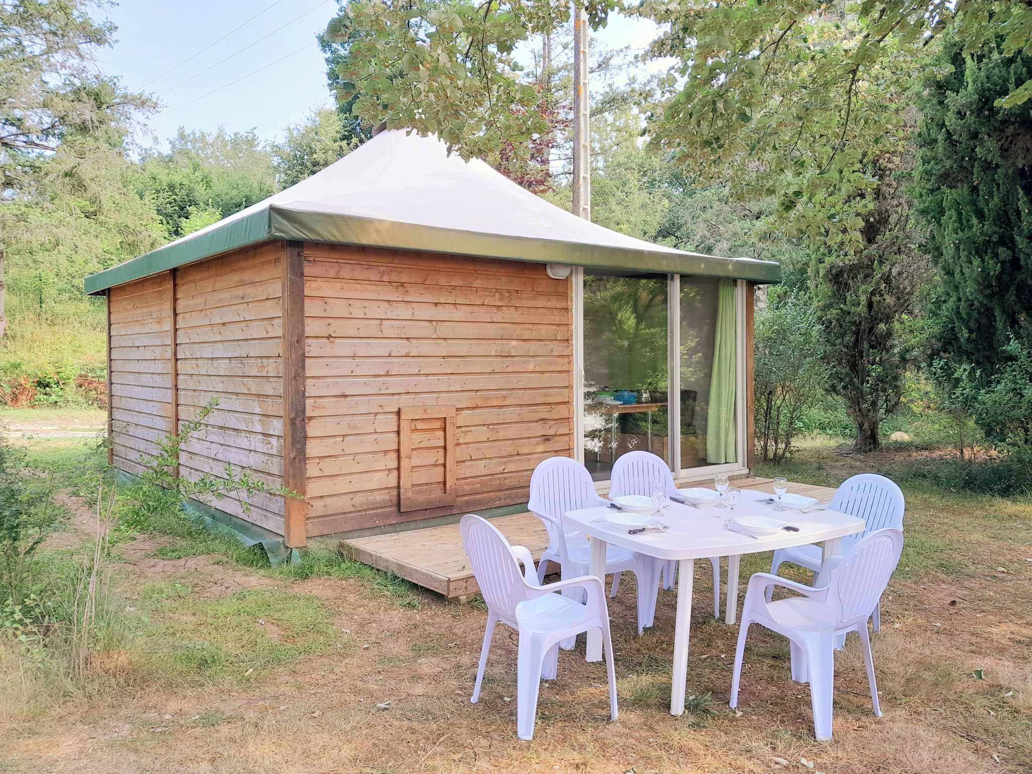 A wooden cabin with a covered patio and white plastic chairs.