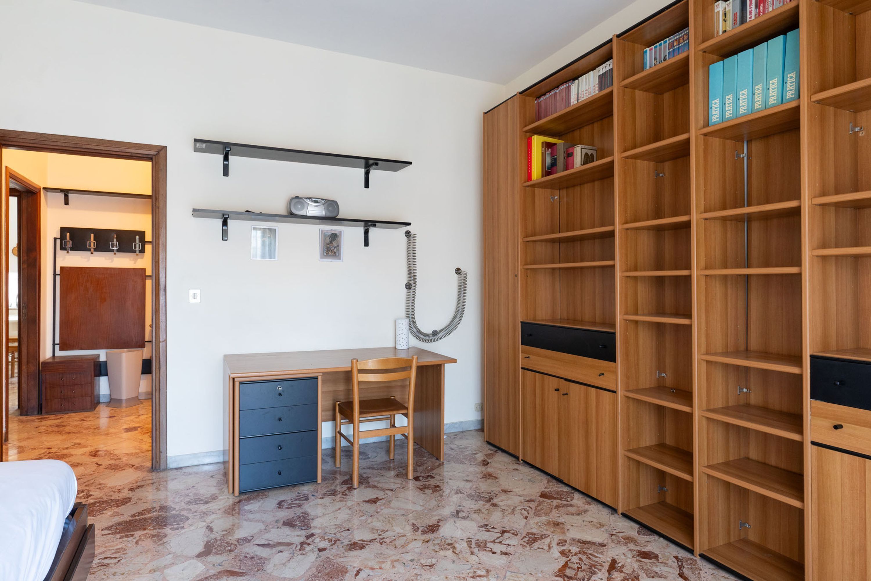 Een slaapkamer met een bed, een bureau, een stoel, een kledingkast en een boekenkast.