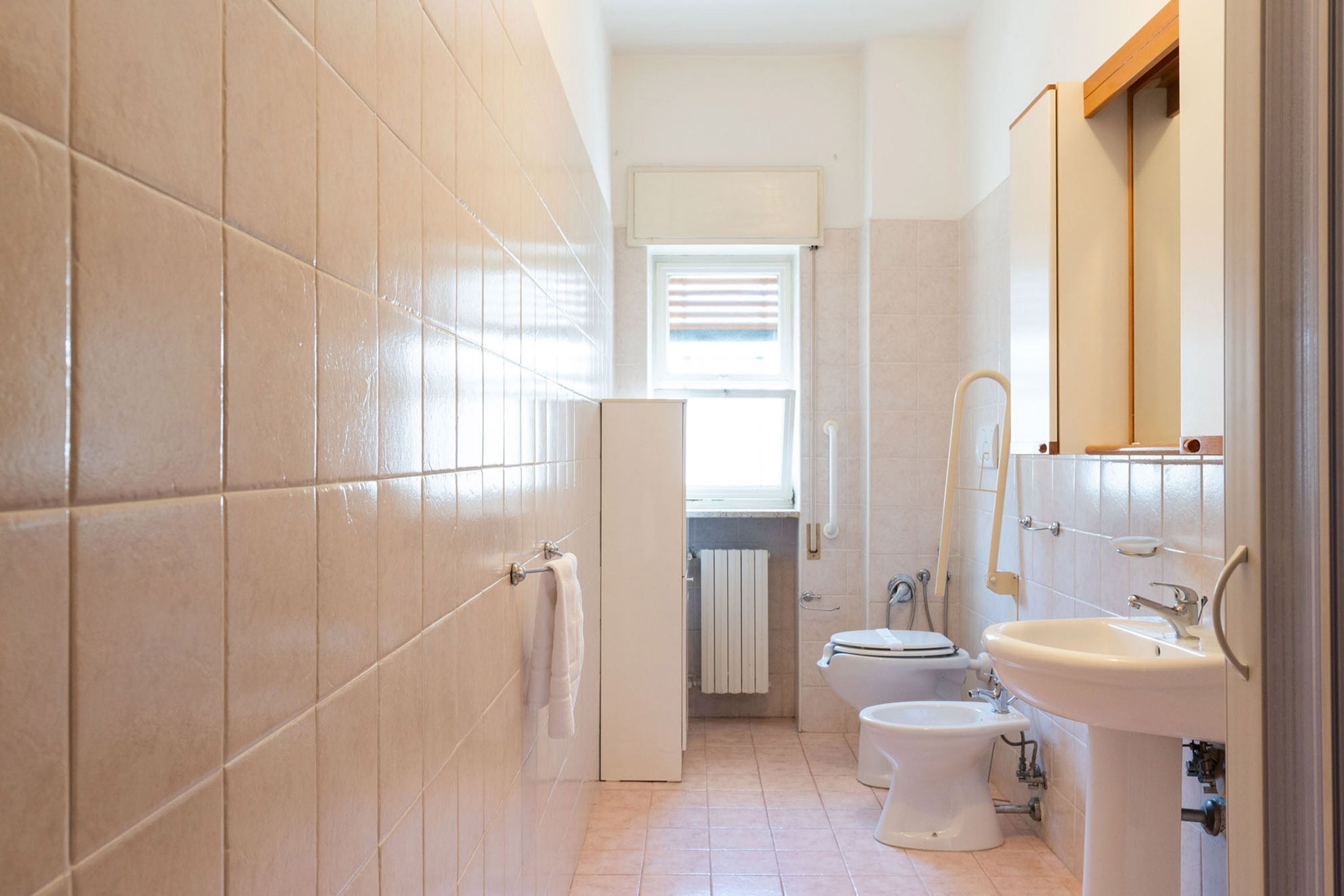 A bathroom with beige tiles, a toilet, bidet, and a sink.