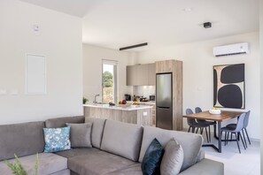 A modern kitchen with a central island, a dining area with a wooden table and chairs, and a living area with a sofa and cushions. - Protaras Mythical Seas (Paralimni)