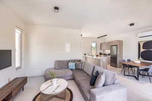 A modern living room with a sectional sofa, a coffee table, and a dining area with a wooden table and chairs. - Protaras Mythical Seas (Paralimni)
