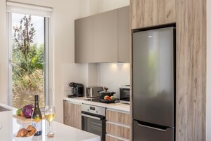 Una cocina moderna con refrigerador de acero inoxidable, armarios de madera, horno empotrado y ventana con vistas a la vegetación.