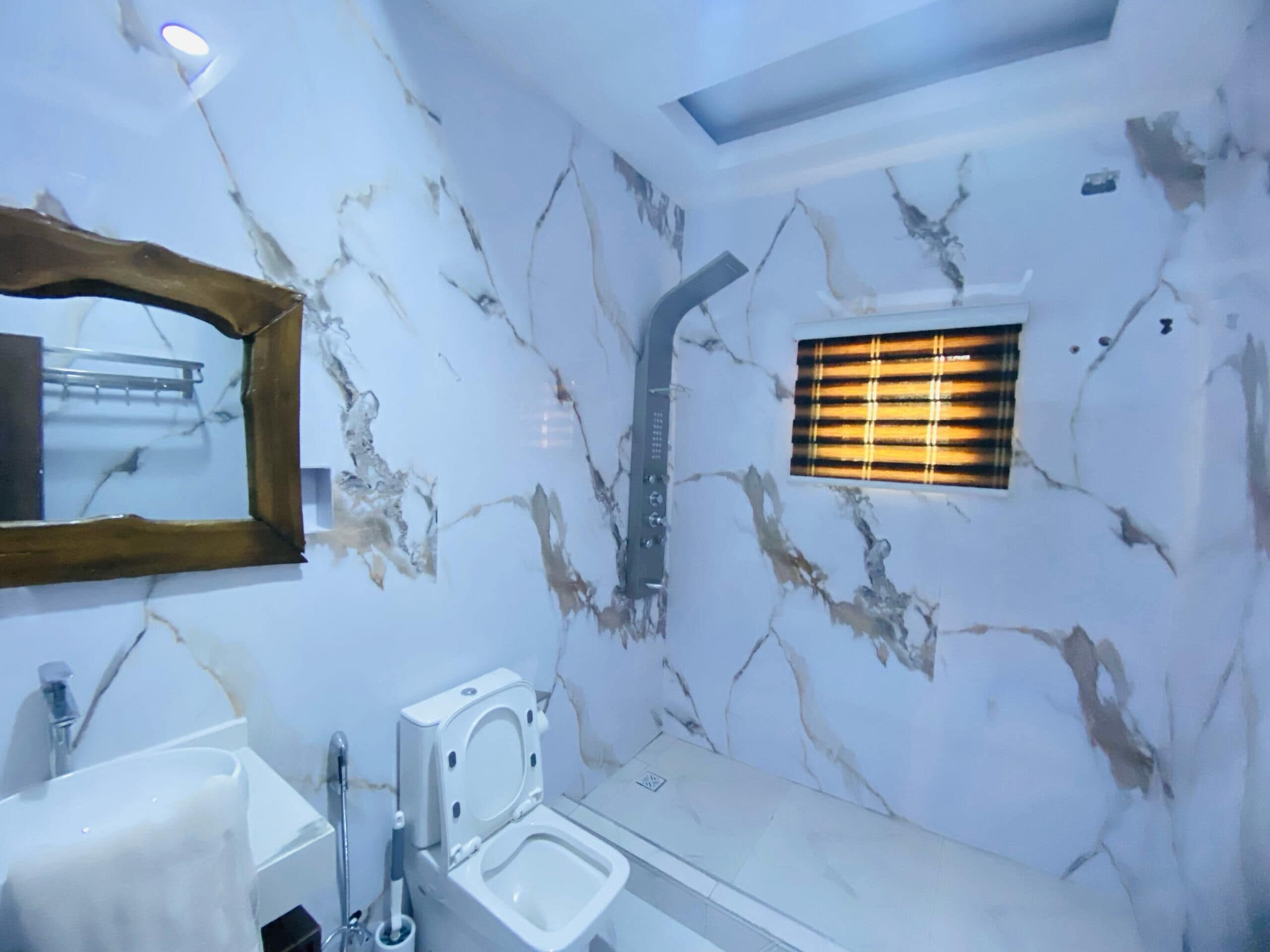 Une salle de bain avec un mur en marbre, des toilettes, un lavabo, un miroir et une douche.