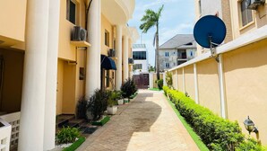 A narrow, paved pathway flanked by buildings with air conditioning units and satellite dishes. - Presken Oniru (Lagos)
