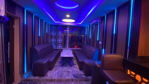 A hallway with blue ambient lighting, a central seating area with a table, and a view through a glass partition. - Presken Oniru (Lagos)