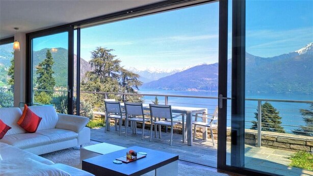 A modern living room with a large glass door leading to a balcony overlooking a lake and mountains. - FABULOUSLY LOCATED WITH VIEWS OF LAKE COMO WITH A HEATED POOL (Menaggio)