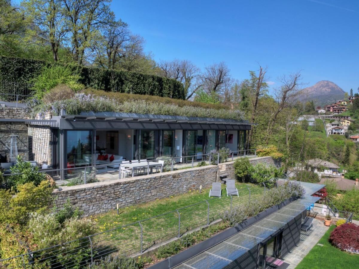 Une maison moderne dotée d’une façade en verre, de murs en pierre et d’un jardin sur le toit.