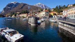 A marina with boats docked, a stone tower, and buildings with red roofs. - FABULOUSLY LOCATED WITH VIEWS OF LAKE COMO WITH A HEATED POOL (Menaggio)