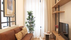 A living room with a brown sofa, a tall bamboo plant, a small table with a candle, and a television on a wooden stand. - Modern Flat Near Trindade by LovelyStay (Porto)