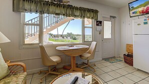 A kitchen with a dining table, chairs, a refrigerator, and a TV. - Directly on the Gulf - Unit  2  - 1 Bedroom - Ground Floor - Sleeps up to 4 (Venice)