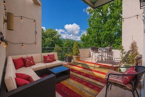 A balcony with a sofa, chairs, a coffee table, and a colorful rug.